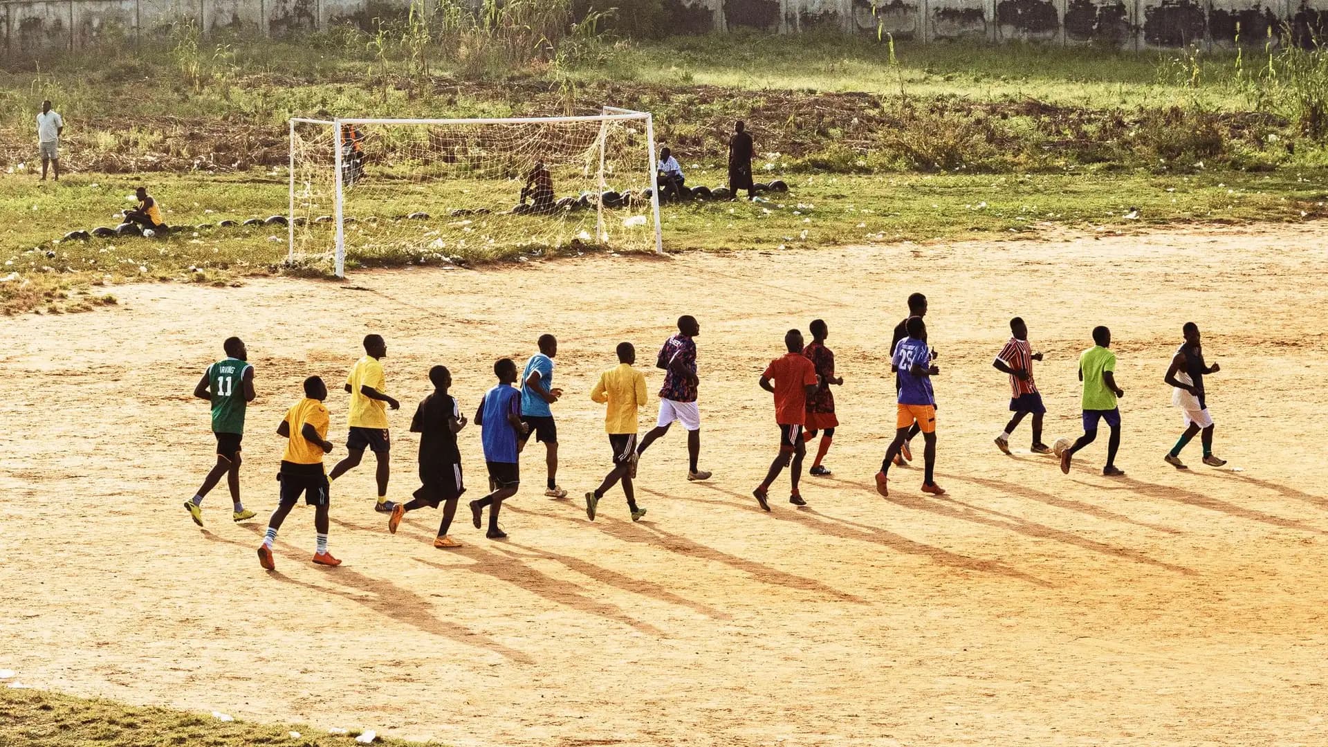 Groupe de jeunes joueurs à l'entraînement sur un terrain de terre, en fin de journée